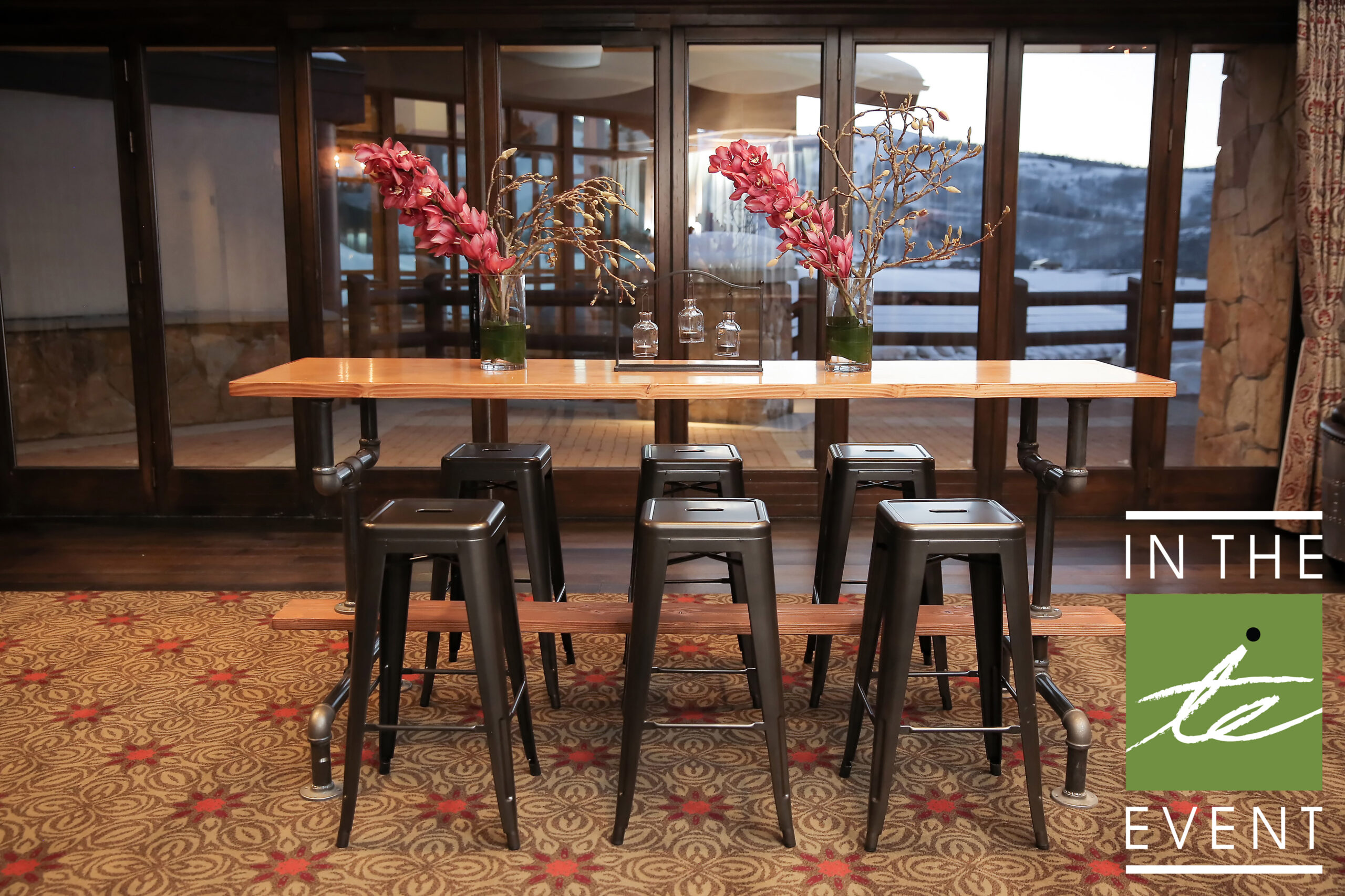 Industrial-style highboy table with black stools and floral centerpieces at an event venue.