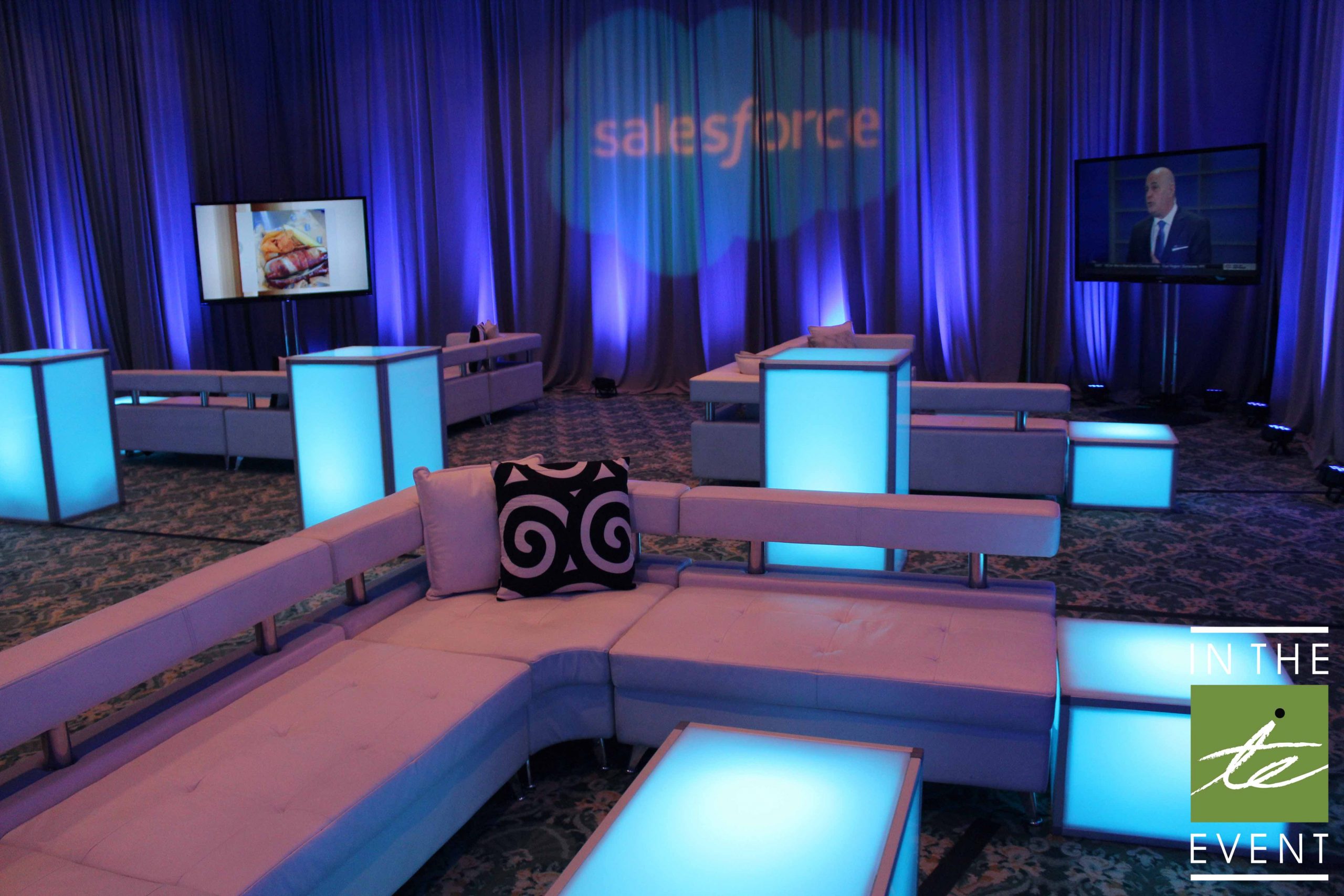 Salesforce lounge setup with glowing LED tables, modular seating, and branded uplighting in blue tones.