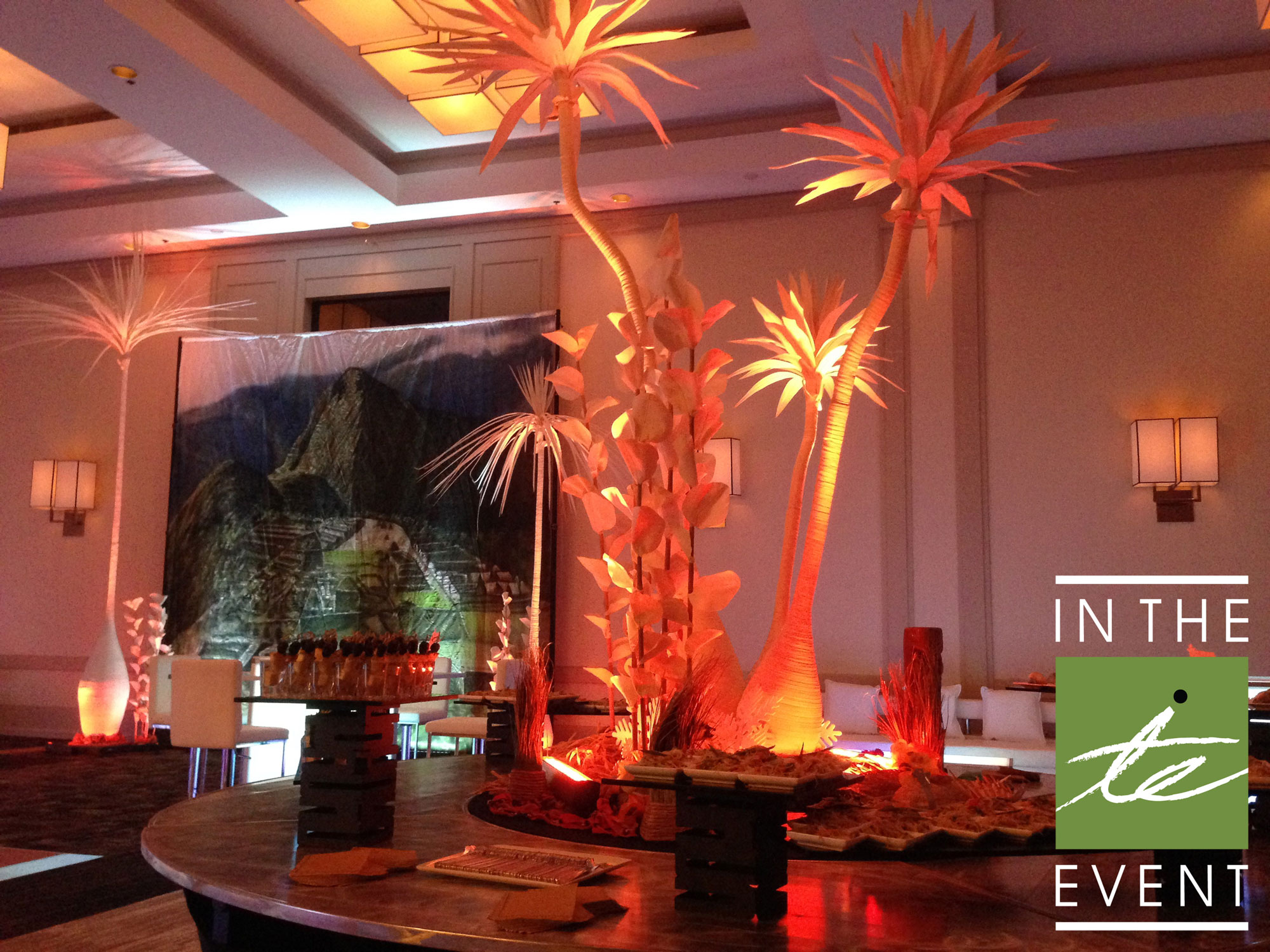 Illuminated palm tree event decor with scenic backdrop and themed lounge seating for tropical corporate party
