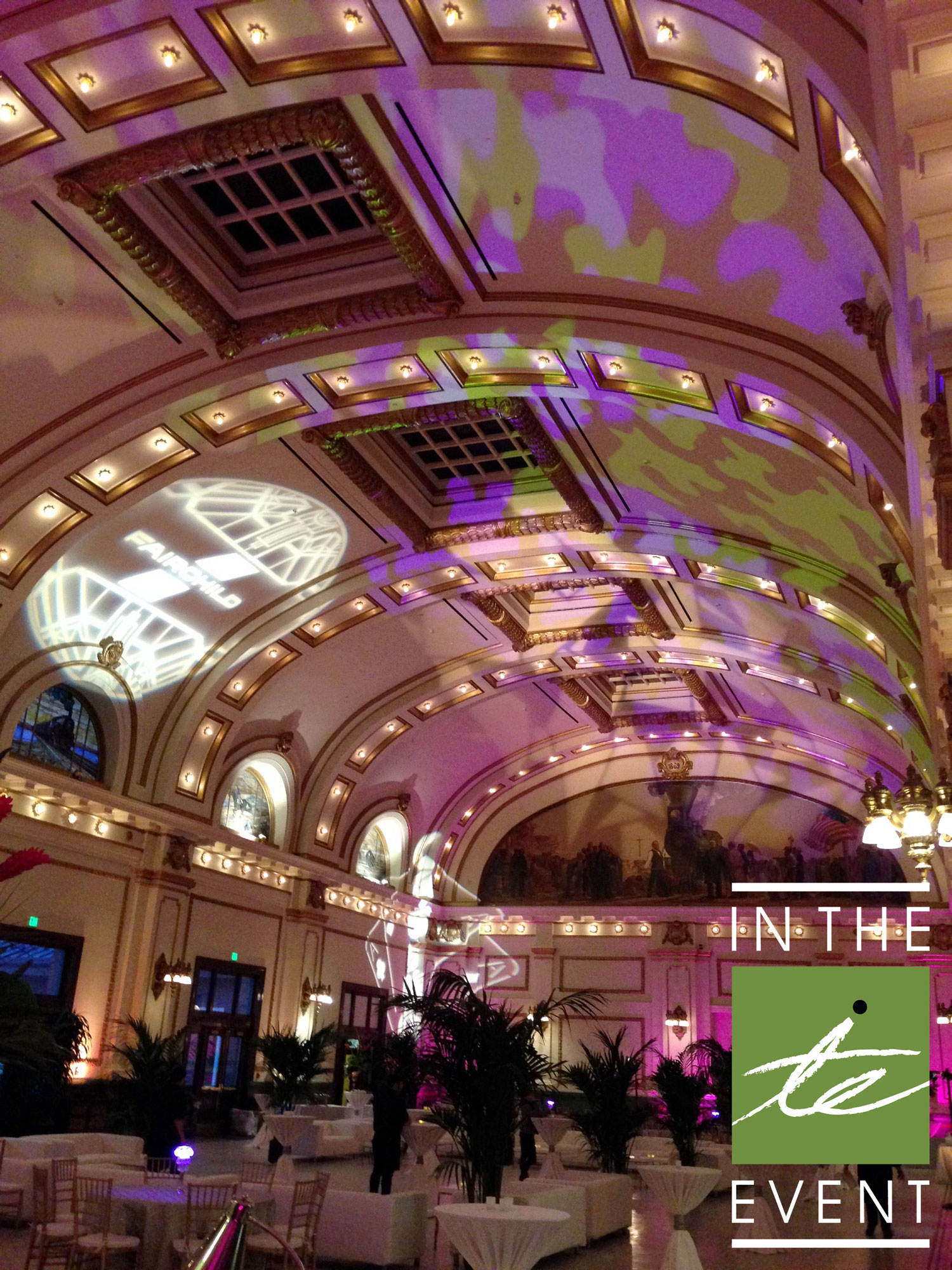 Elegant ballroom event setup with branded gobo projection on the ceiling, purple uplighting, and lounge furniture