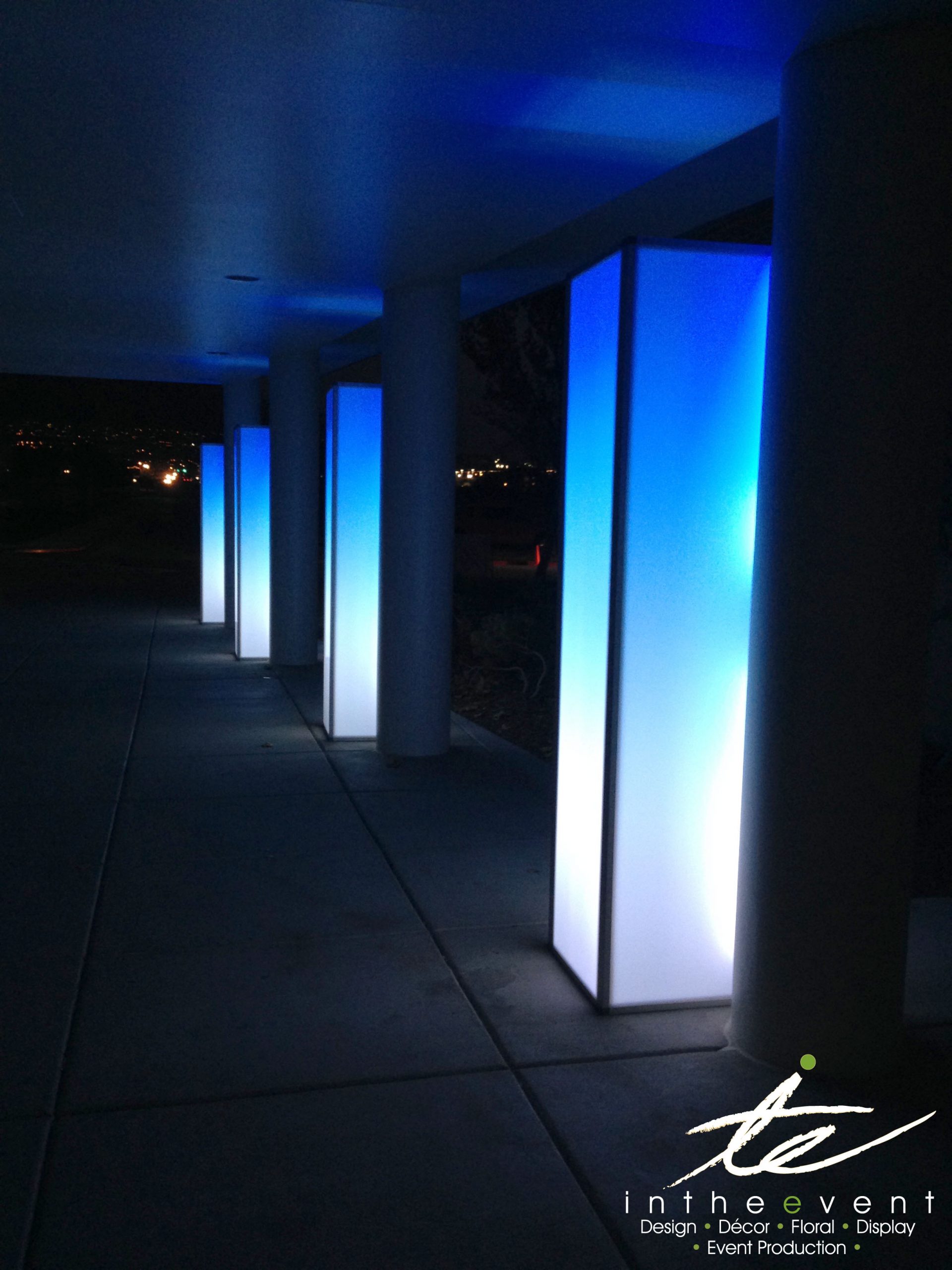 Glowing blue LED towers set up along an outdoor walkway, providing elegant event lighting and modern decorative structures.