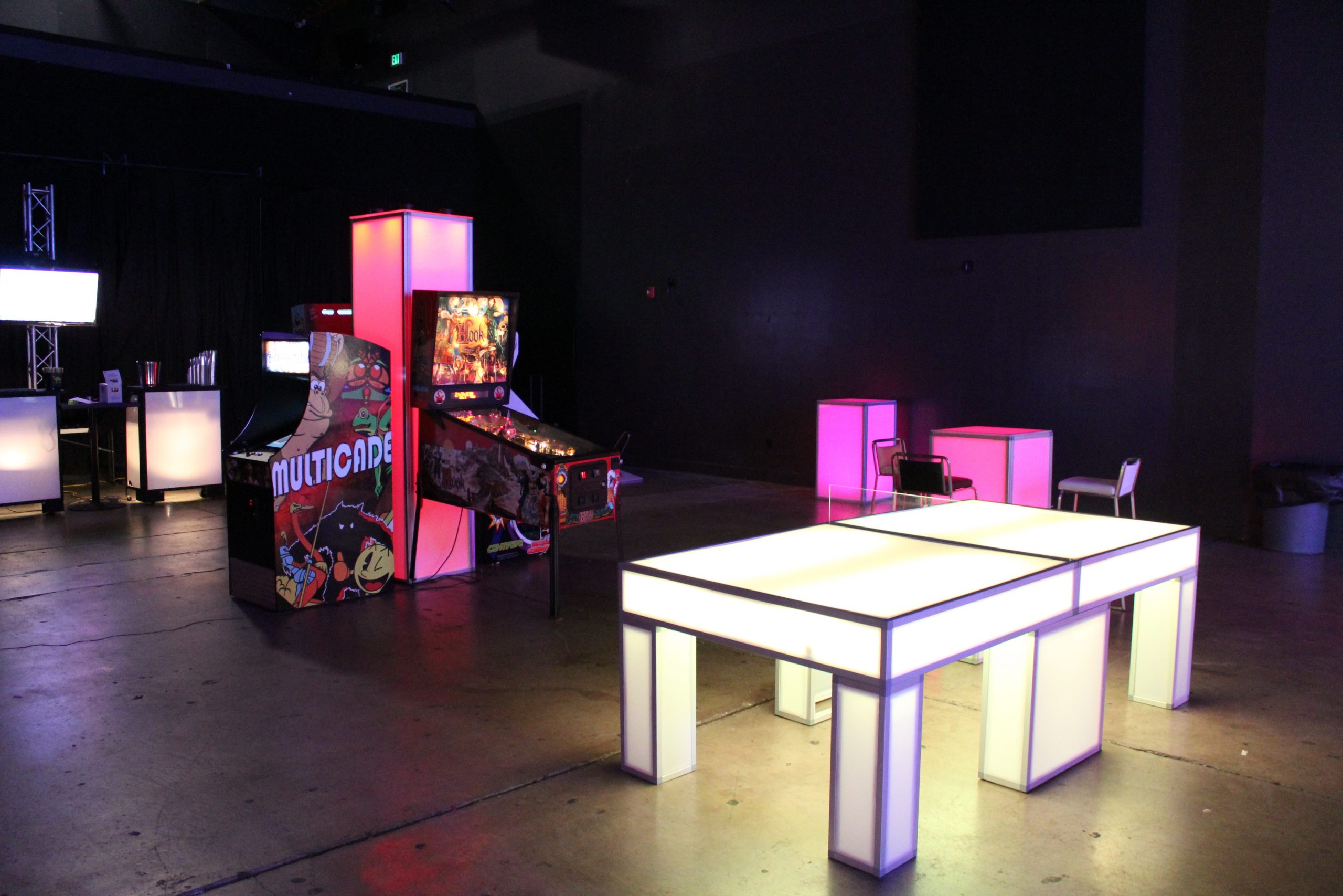 Light-up ping pong table rental with glowing LED panels alongside arcade and pinball machines at an In The Event setup.
