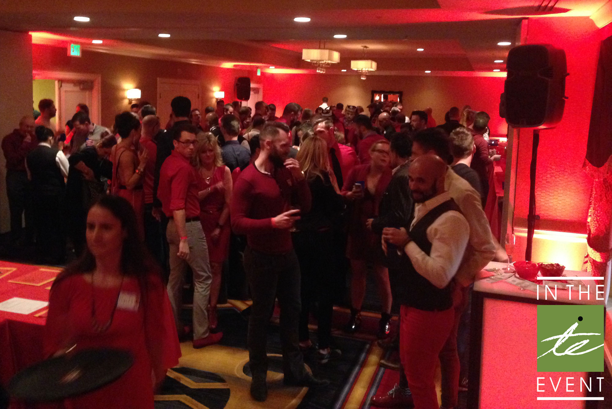 Crowd gathered at red-themed party with dramatic red lighting, LED furniture, and event decor by In The Event.