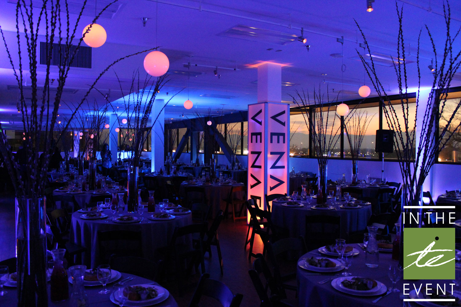 Corporate event hallway with glowing LED cocktail tables and blue uplighting.