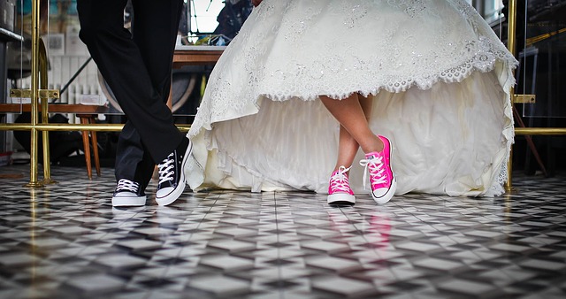 Bride in lace wedding gown with pink sneakers and groom in tuxedo with black sneakers, showcasing a playful and modern wedding event style.