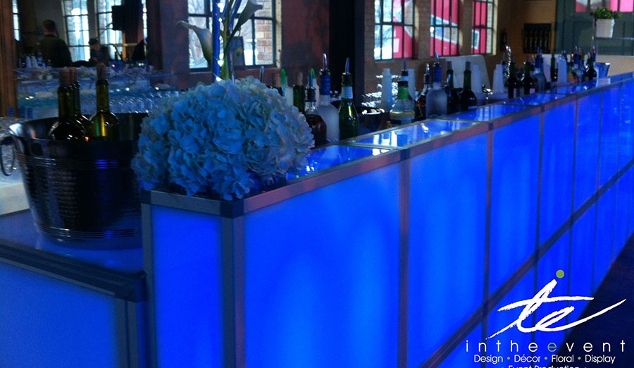 Illuminated LED bar rental with drinks and floral decor, perfect for galas, trade shows, and corporate events with modular event structures and production.