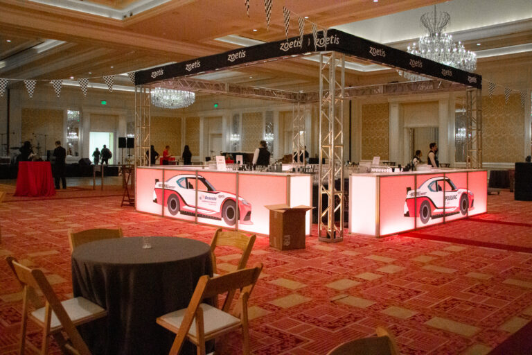 LED-lit bar with race car graphics and Zoetis branding, surrounded by black-and-white checkered bunting in a ballroom setting.
