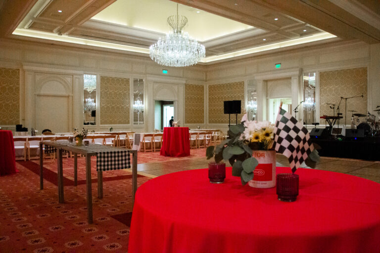 Elegant ballroom with red tablecloths, checkered flag centerpieces in vintage oil cans, and a chandelier overhead at a Zoetis event.