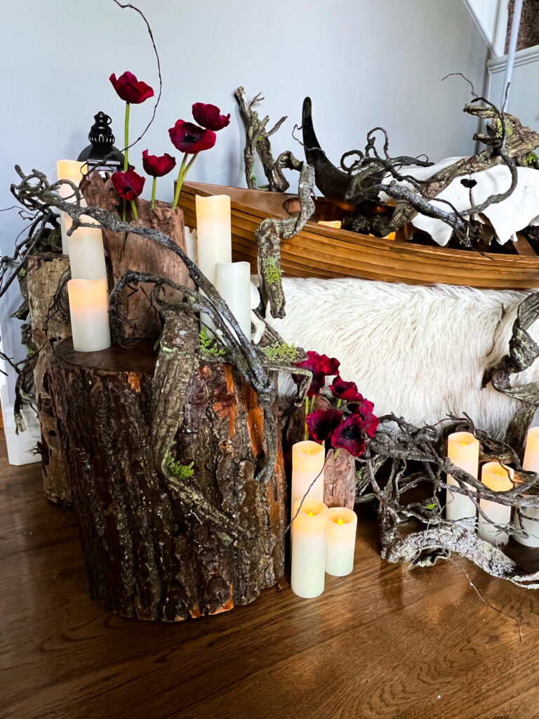 Detailed indoor decoration featuring wood slices as candle holders, white pillar and votive candles, dark red flowers, moss, branches, a lantern, and faux fur.