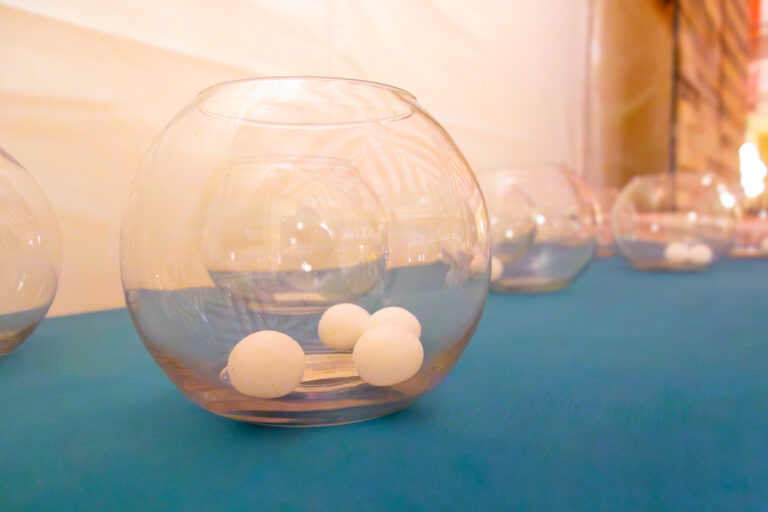 Glass fishbowls lined up on a table with white ping pong balls inside at a carnival game booth
