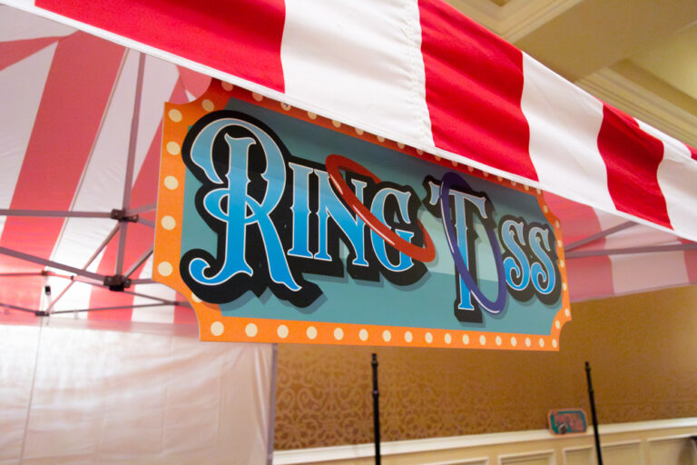 Colorful "Ring Toss" carnival game sign hanging under a red and white striped tent