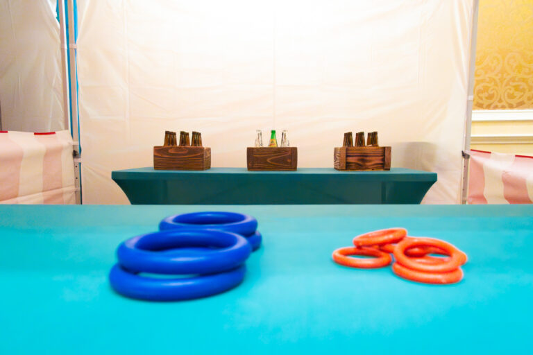 Colorful red and blue rings in the foreground with wooden crates of glass bottles in the background, set on teal tables.
