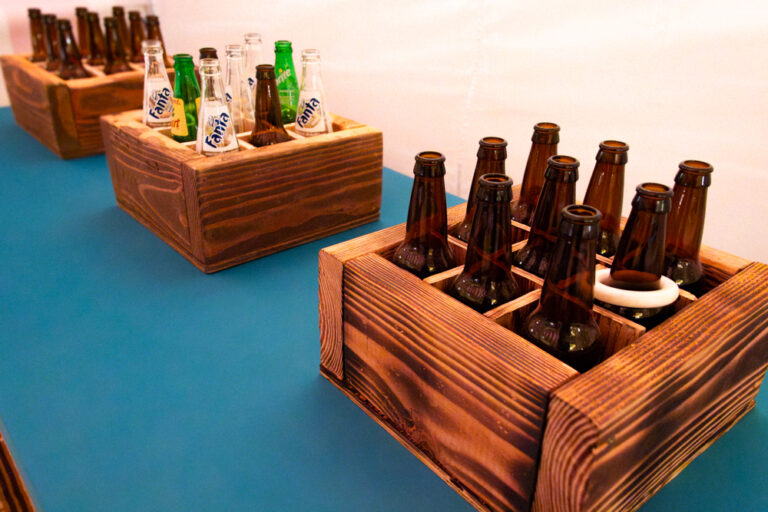 Glass bottle ring toss game with brown and green bottles arranged in rustic wooden crates on a teal table.