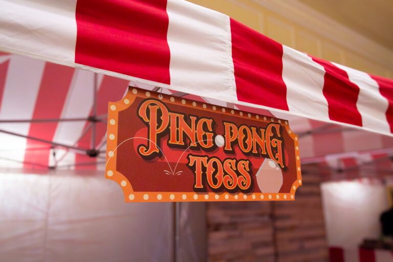 Vintage-style Ping Pong Toss sign hanging under a red and white carnival tent at a themed event