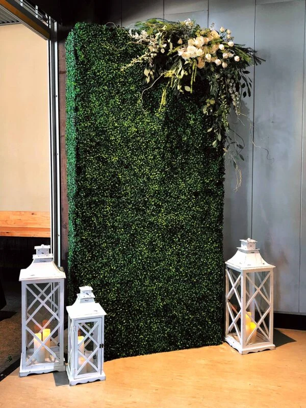 Artificial greenery wall with white lanterns and floral arrangement