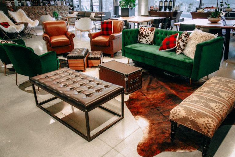 Western-style lounge area with green velvet couch, leather armchairs, patterned benches, and rustic accents including a cowhide rug and vintage trunk coffee table.