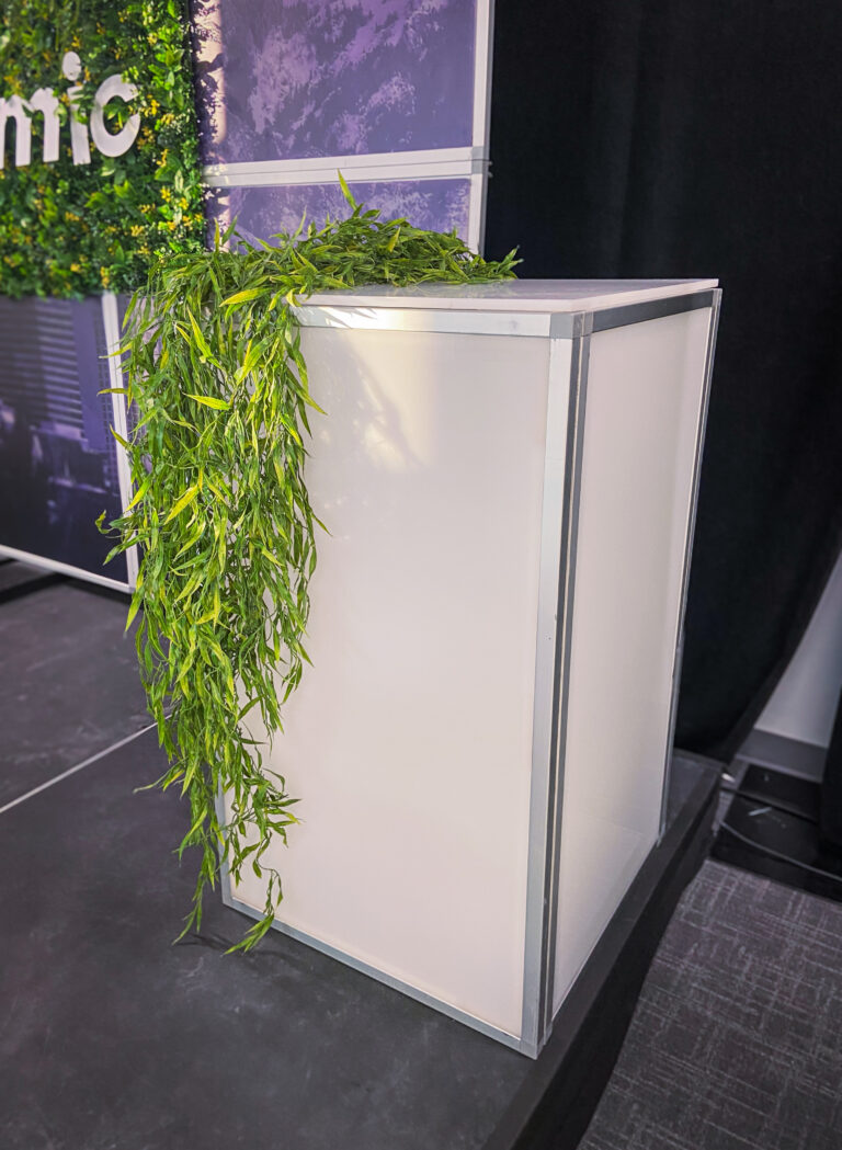 Modern white podium with cascading greenery detail on stage at Atomic-branded event.