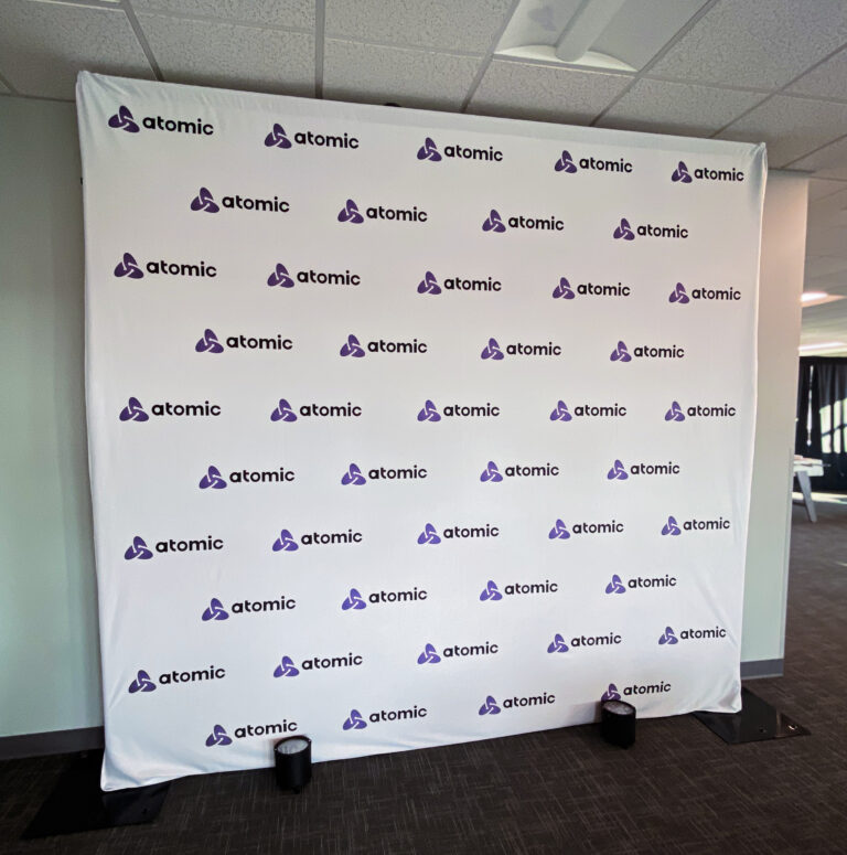 White Atomic-branded step-and-repeat backdrop with purple logos in a grid pattern.