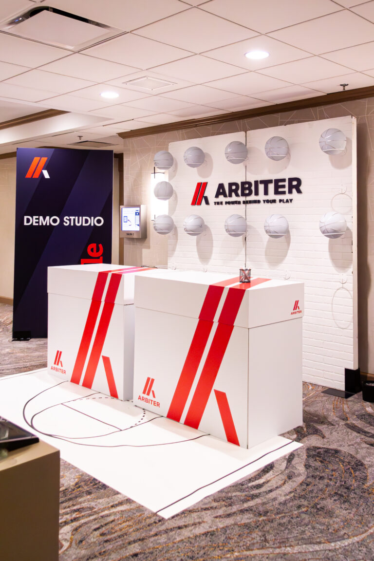 Branded registration counters with a basketball court floor graphic and a backdrop of silver basketballs and Arbiter signage.
