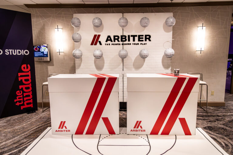 Branded registration counters with a basketball court floor graphic and a backdrop of silver basketballs and Arbiter signage.