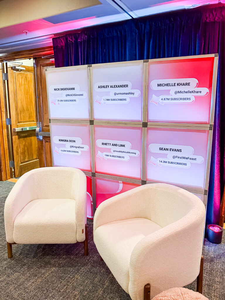 A branded influencer display wall with creator names, flanked by modern cream lounge chairs and pink lighting.