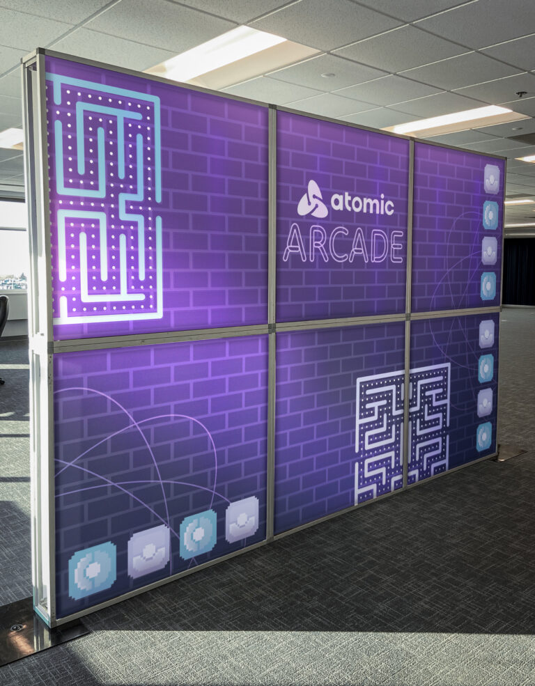 Atomic-branded arcade wall with pixelated graphics and purple maze design on a modular frame.