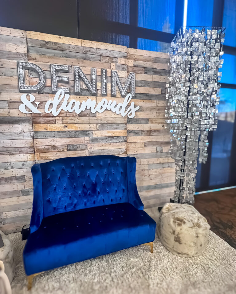 Denim and Diamonds themed photo backdrop with blue velvet loveseat, wood panel wall, and crystal chandeliers.