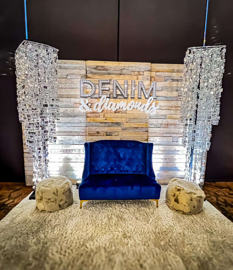 Denim and Diamonds themed photo backdrop with blue velvet loveseat, wood panel wall, and crystal chandeliers.