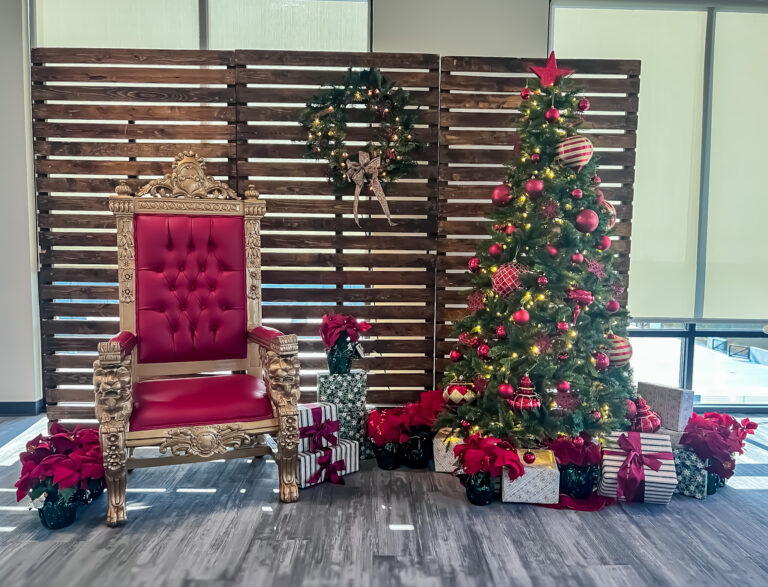 Holiday photo setup with a red and gold throne, decorated Christmas tree, and wrapped gifts.