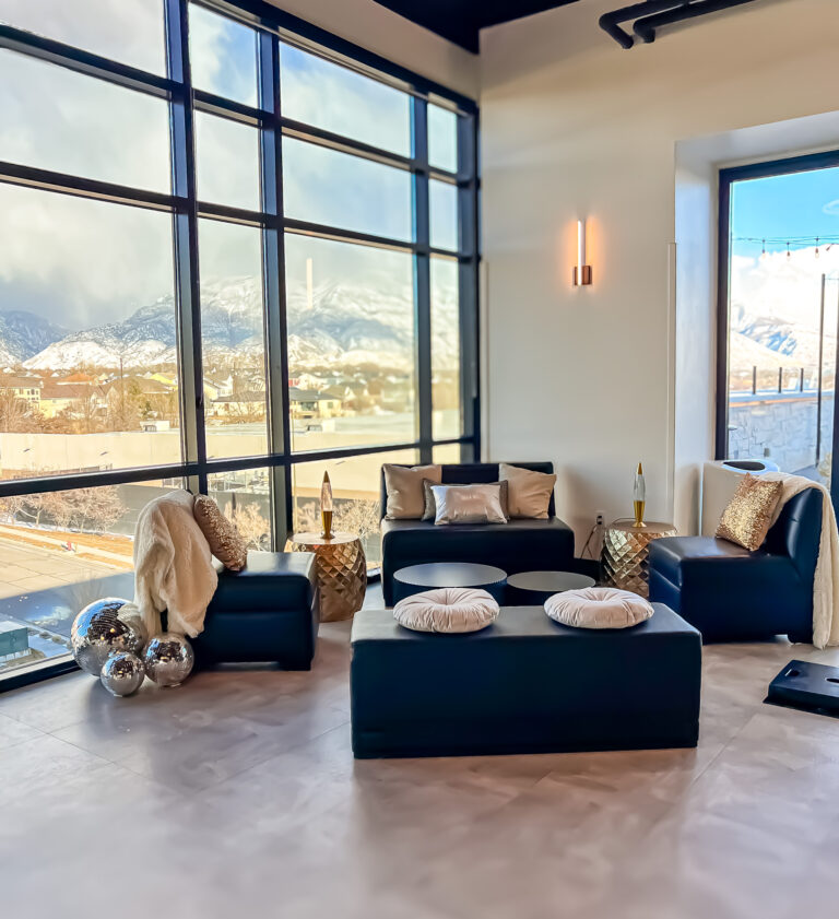 Modern lounge seating with gold pillows, disco balls, and floor-to-ceiling windows overlooking snowy mountains.