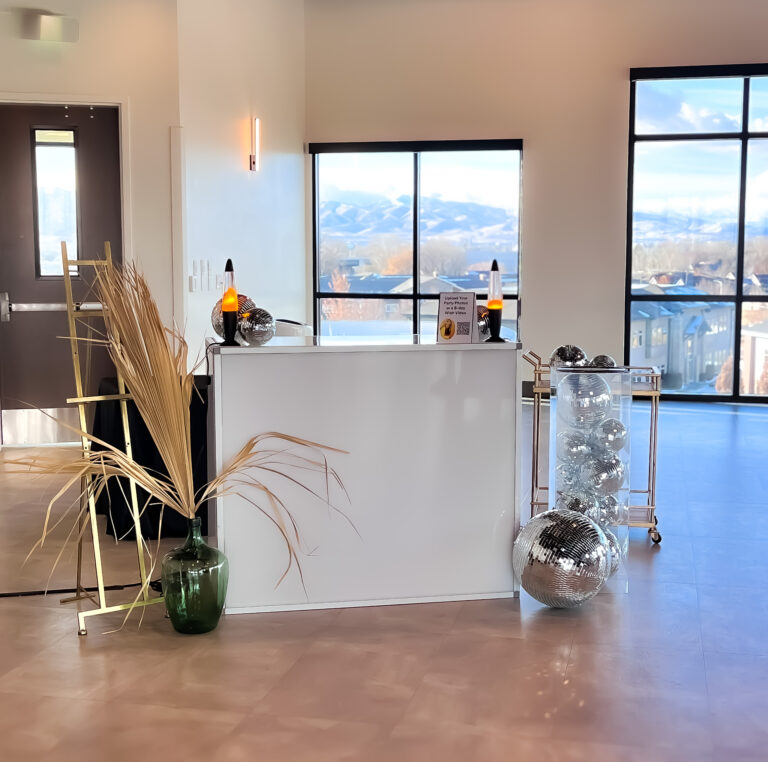 Modern event check-in table with lava lamps, disco balls, and dried palm decor.