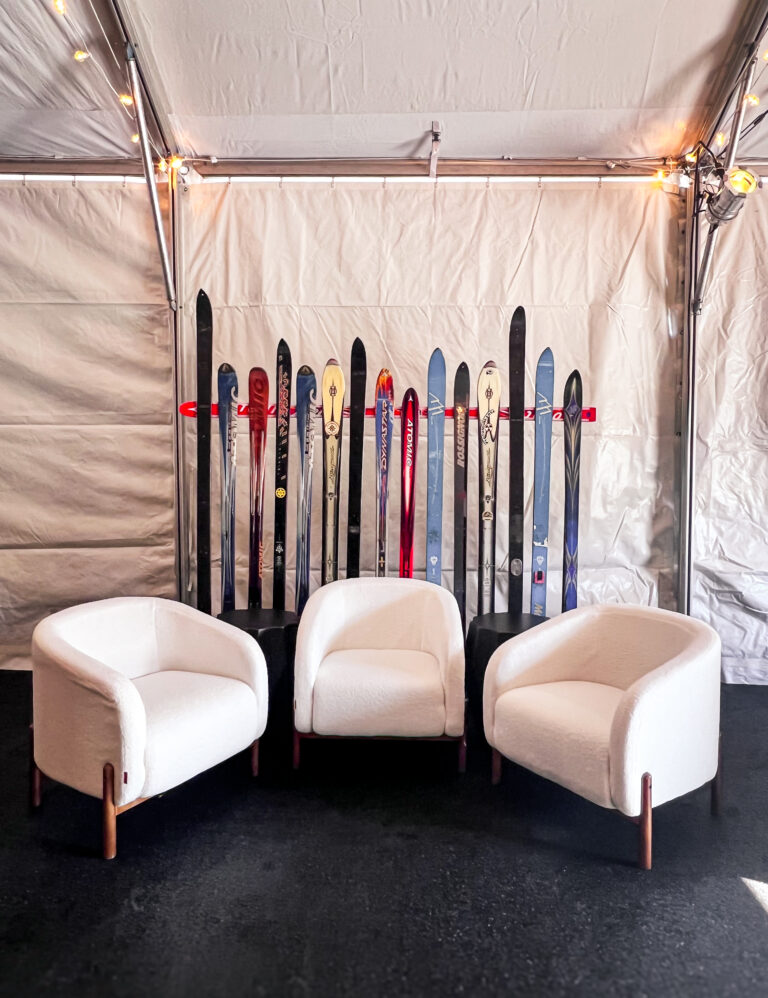 Lounge setup with three white boucle chairs and a vintage ski backdrop inside a tented event space.