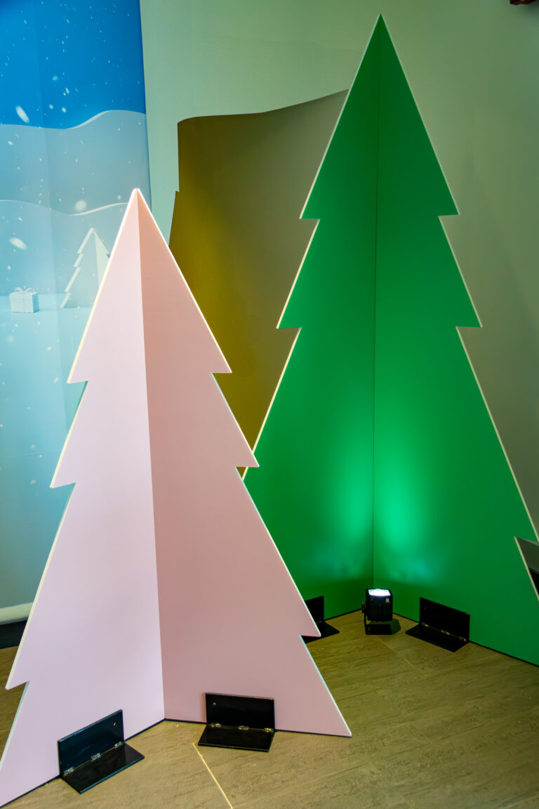 Freestanding pastel pink and green wooden Christmas trees lit from below, set against a winter-themed event backdrop.