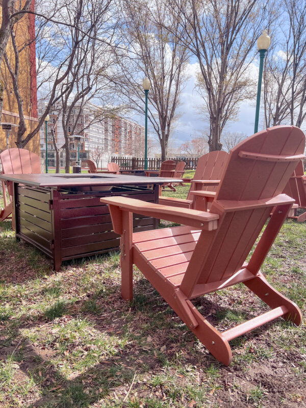 Folding Adirondack chair near a fire table in a shaded park event lounge setup.