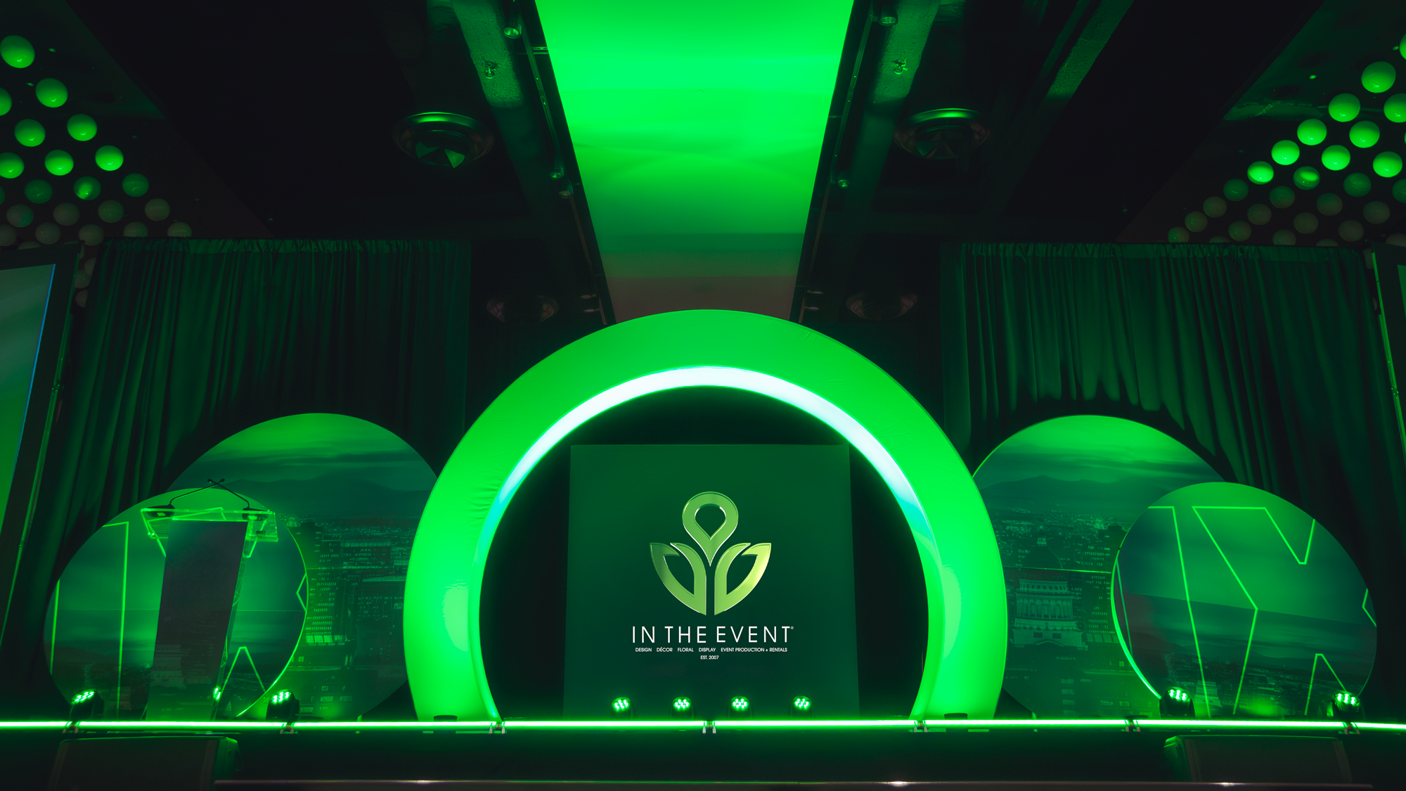 Branded stage design with green LED arch and circular backdrops for In The Event.