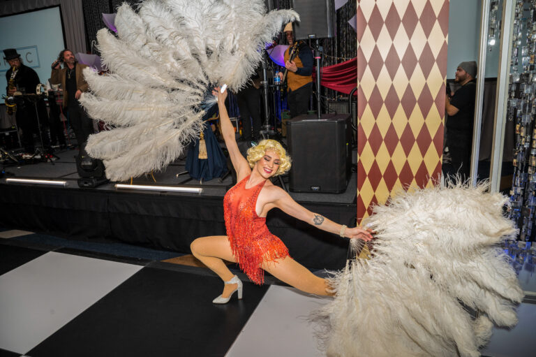 Dancer in red costume performs with large white feather fans at the 2024 SILAC Insurance Gala