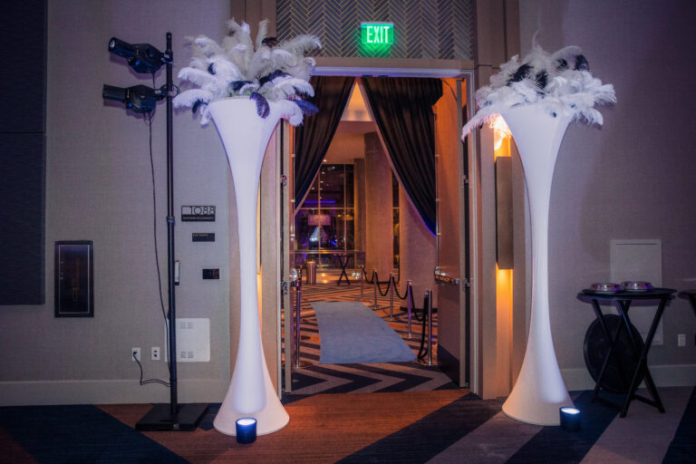 Tall white vases with feather plumes flank the blue carpet entryway at the 2024 SILAC Insurance Gala