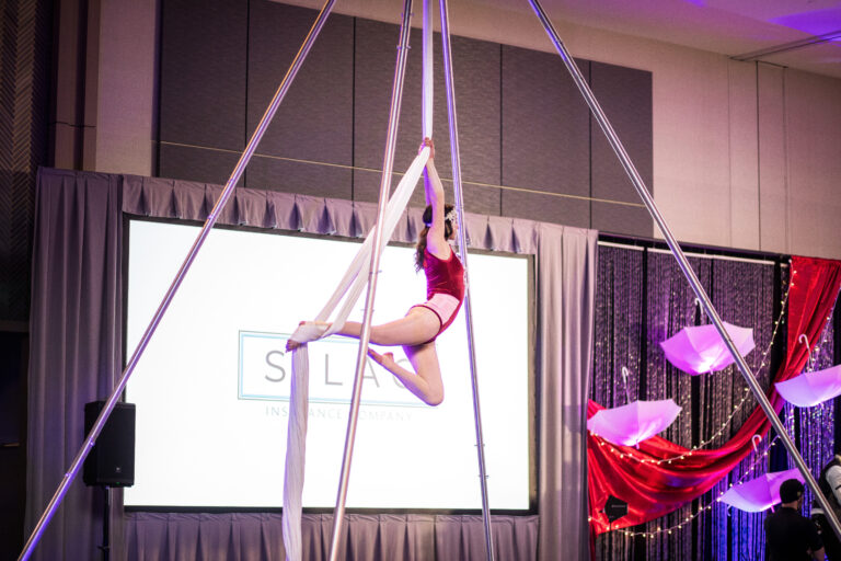 Aerialist in red costume performs on white silks at the 2024 SILAC Insurance Gala