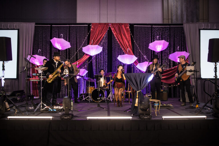 Live band performs on a decorated stage with umbrellas and red drapery at the SILAC Insurance Gala 2024