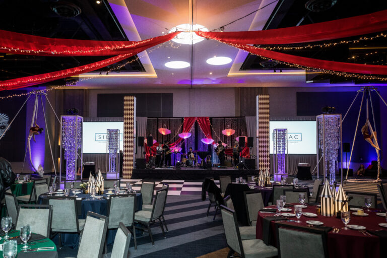 Main stage view with umbrella backdrop, live band, and aerialist rigs at the SILAC Insurance Gala 2024