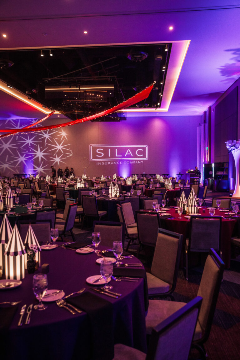 Striped centerpiece decorations and uplighting with SILAC Insurance Company projection on the wall at SILAC Gala 2024