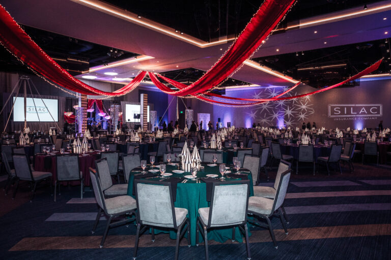 Wide view of banquet hall with red ceiling drapery, themed centerpieces, and branded lighting at the SILAC Insurance Gala 2024