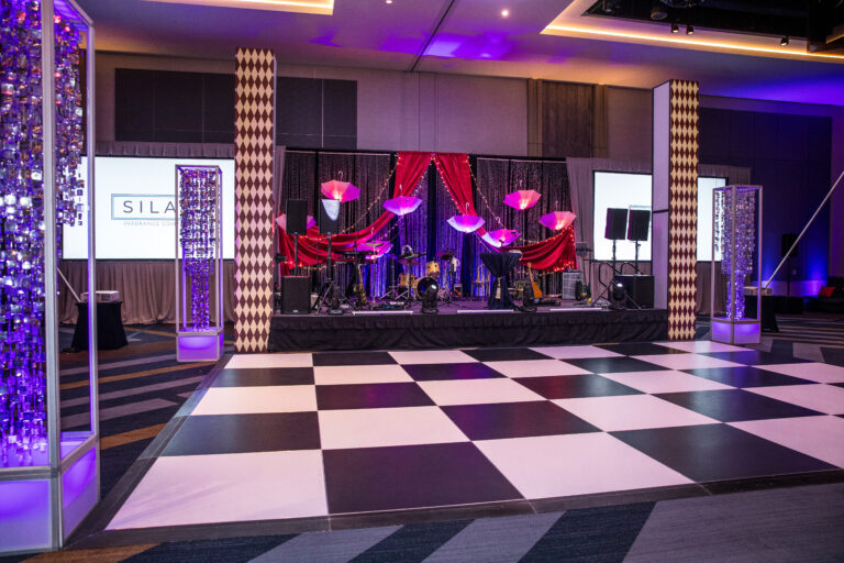 Checkerboard dance floor in front of a stage with drapery, umbrellas, and lighting at the SILAC Insurance Gala 2024