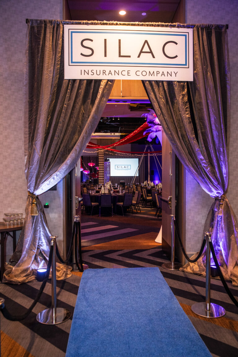 Close-up of SILAC Insurance Gala 2024 entry with silver drapes, branded signage, and blue carpet walkway