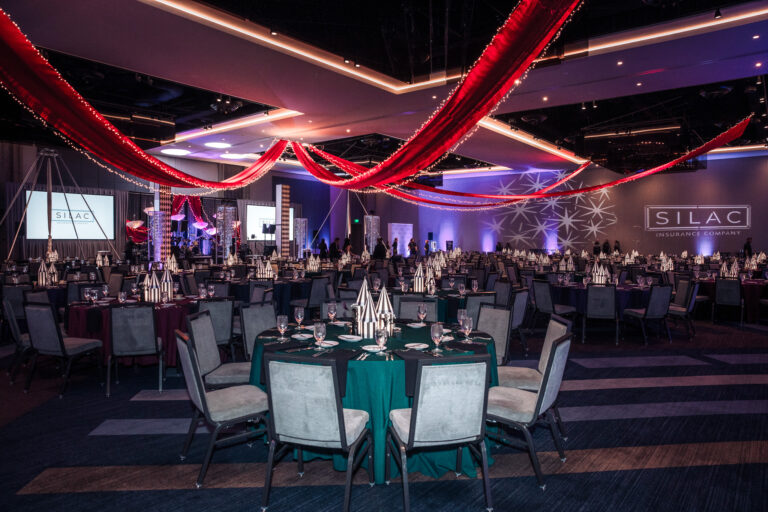 Ballroom decorated with red ceiling drapery, striped centerpieces, and branded lighting at the SILAC Insurance Gala 2024
