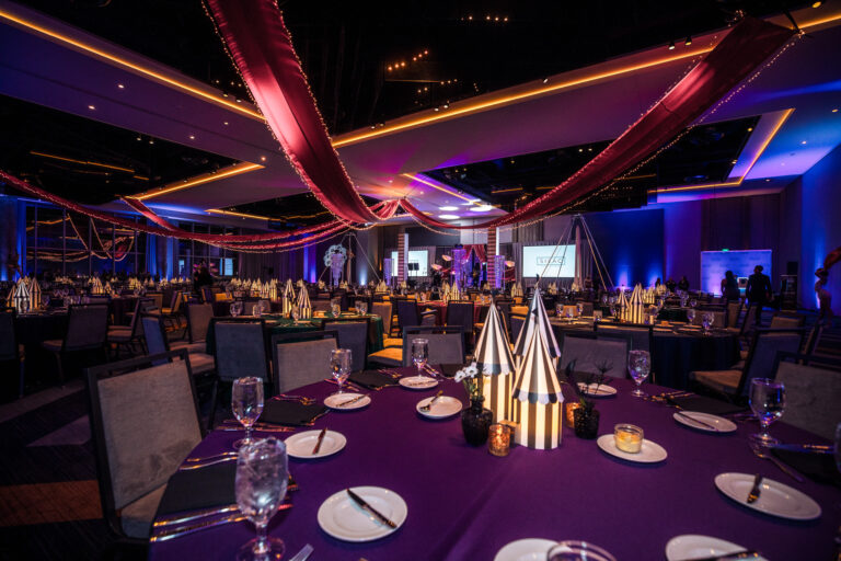 Decorated gala ballroom with striped centerpieces, red ceiling drapery, and colorful uplighting at SILAC Insurance Gala 2024
