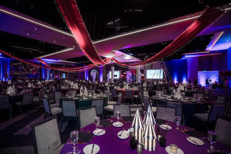Decorated gala ballroom with striped centerpieces, red ceiling drapery, and colorful uplighting at SILAC Insurance Gala 2024