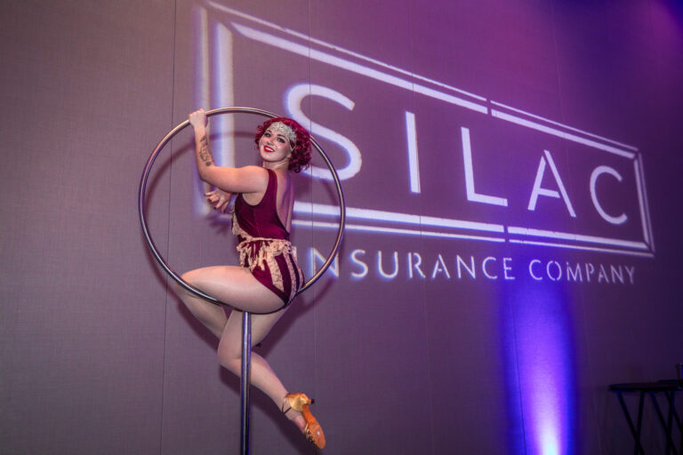 Aerial performer poses on a lyra hoop in front of the SILAC Insurance Company logo projection during the 2024 gala