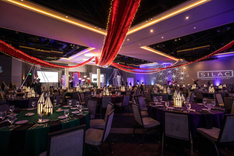 Gala venue decorated with red ceiling drapery, striped centerpieces, and stage lighting at SILAC Insurance Gala 2024