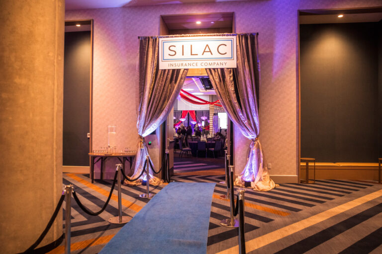Draped entryway with custom signage and uplighting at SILAC Insurance Company gala event